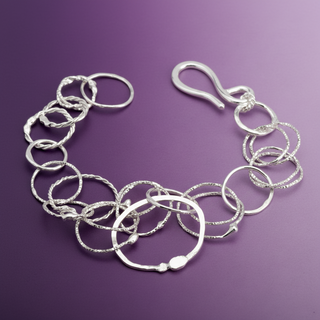 A sterling silver link bracelet with textured and polished circular links, displayed on a smooth purple background.