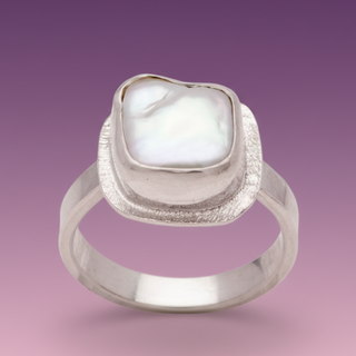 An adjustable silver ring with a large mother of pearl cabochon displayed on a clear holder.
